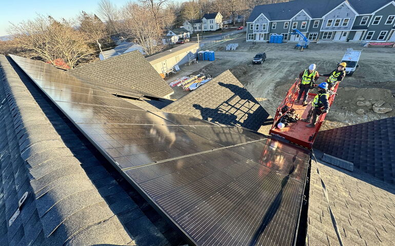 An aerial view shows workers and solar panels on a roof.