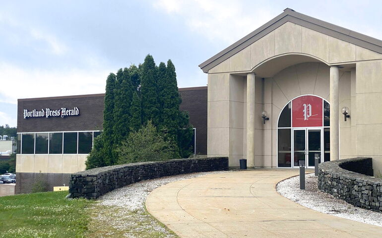 A building has signage on the facade and a curving sidewalk.