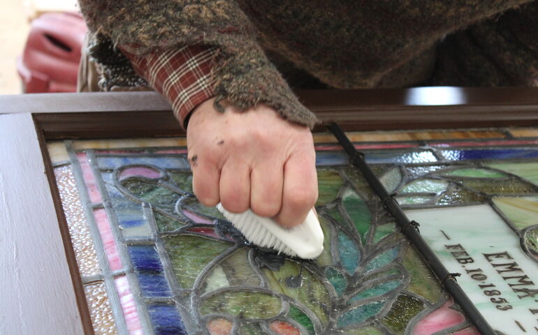 A hand holds a brush against colorful glass.