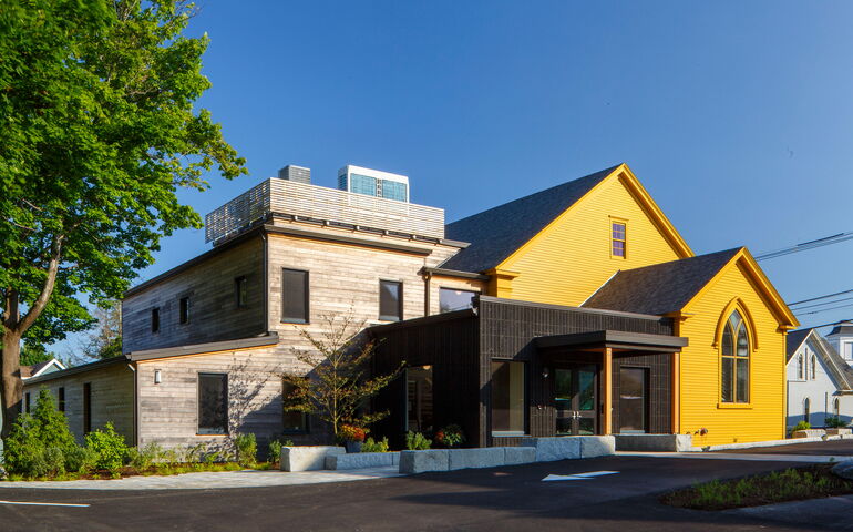 An exterior view of a building with a deep yellow facade and a wood-sided addition.