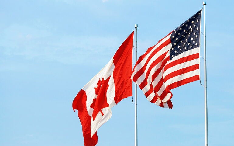 Canada and U.S. flags against a blue sky 
