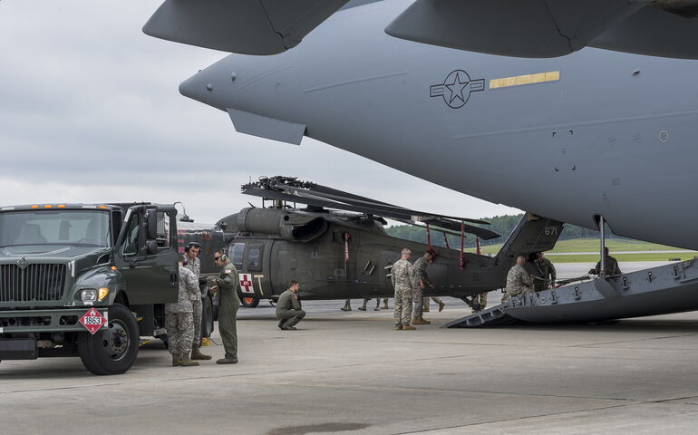 People stand around a gray plane, a  helicopter and a jeep.