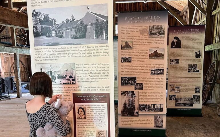 A person holding a teddy bear looks at a sign.