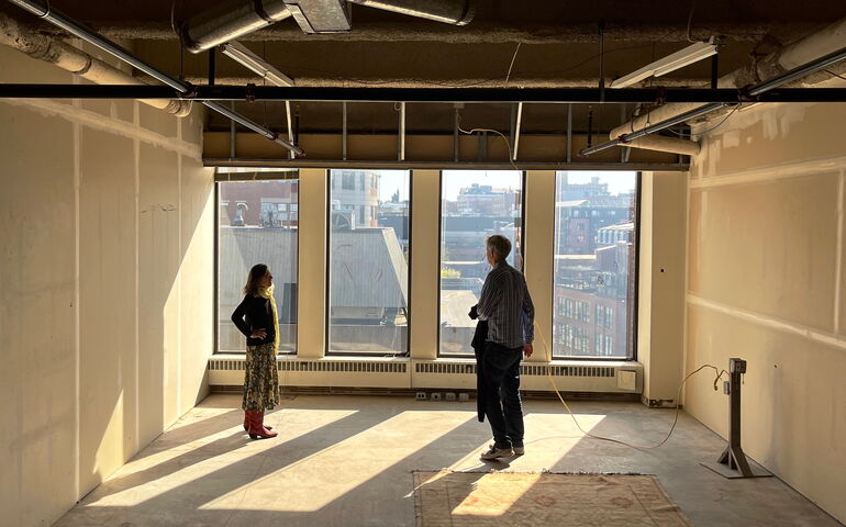 Two people stand in an empty room with a shaft of sunlight.