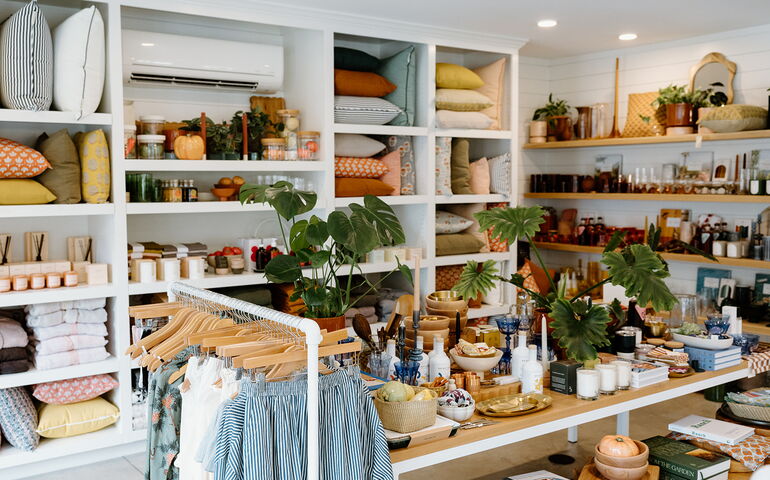 A room has shelves and racks filled with clothes and wares.
