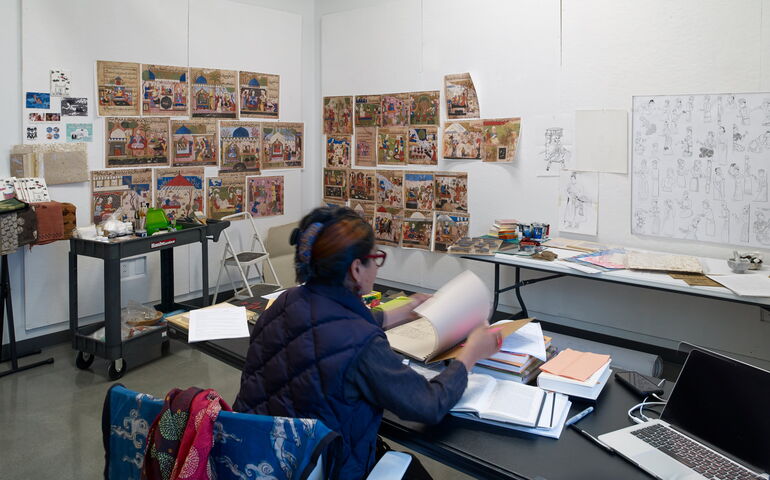 A person sits at a table surrounded by artwork.
