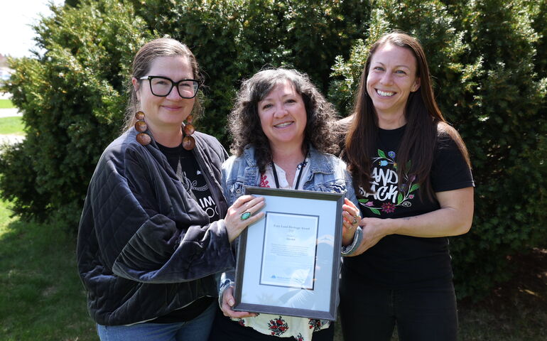 Three people pose with a framed certificate.