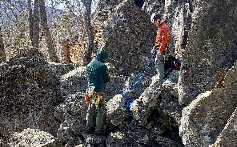 Two people stand on rocks with rope.