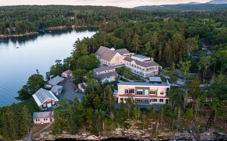 An aerial view shows buildings, woods and water.