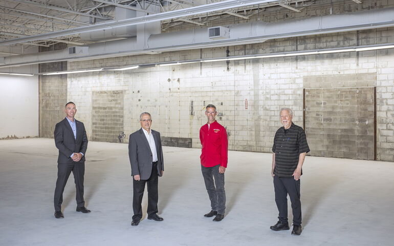 Four people pose in a line in an empty space.