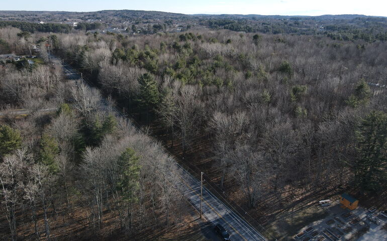 An aerial view shows woods and a road.