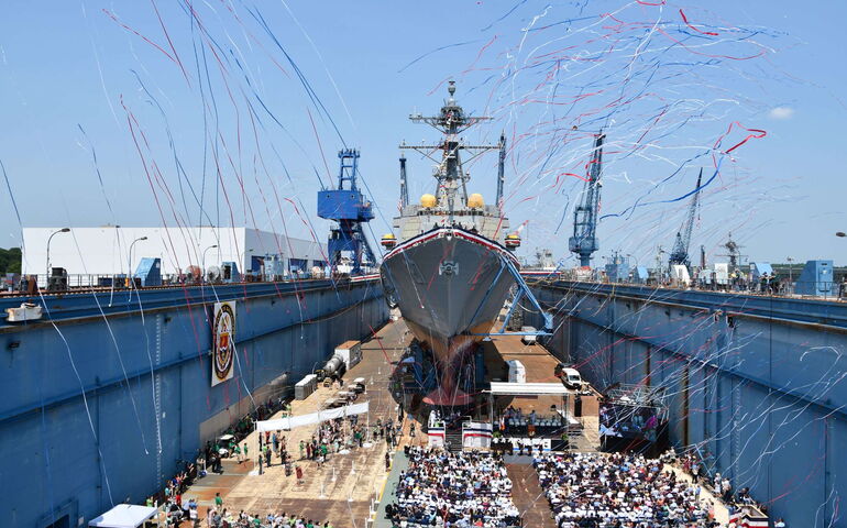 A ship is in a launch area with streamers and people.