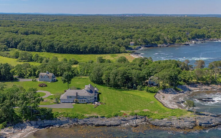 An aerial view shows a house surrounded by lawns and woods.