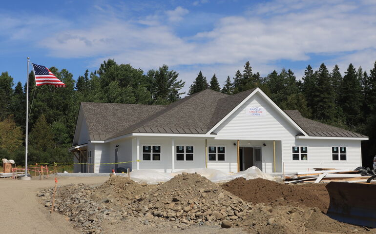 An exterior view of a white-sided building and piles of soil.