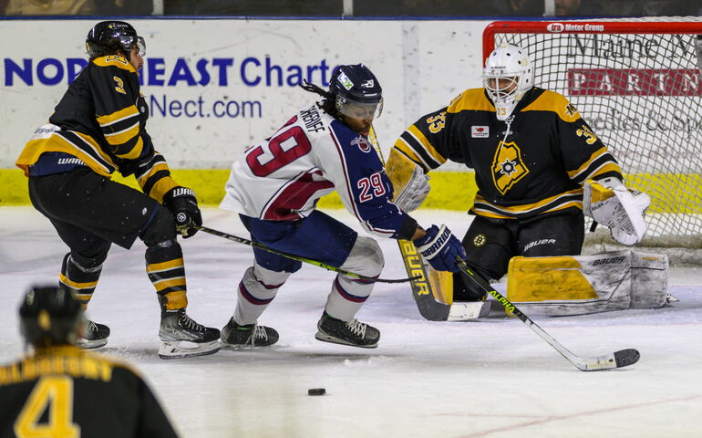Maine Mariners ice hockey action photo of two team members playing defense in front of the goal with an opponent. 