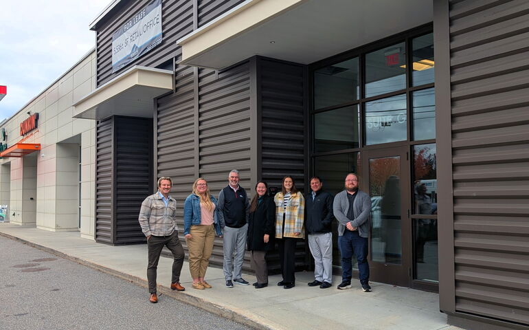 People pose outside of a gray-sided building.