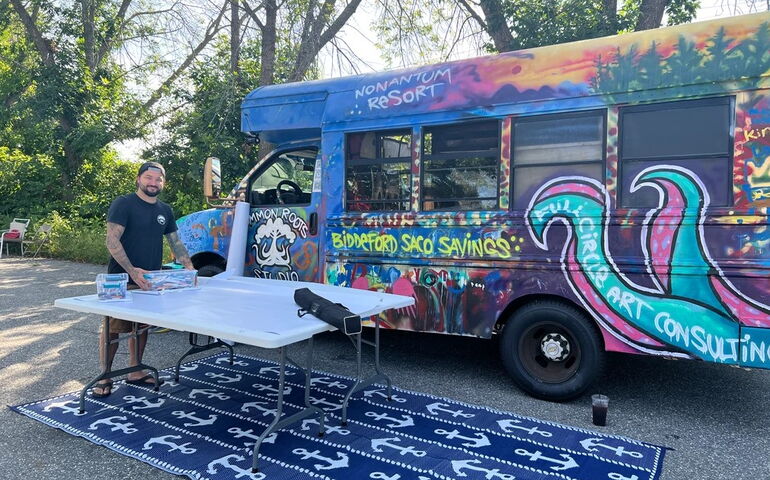 A person stands with a colorfully painted bus.