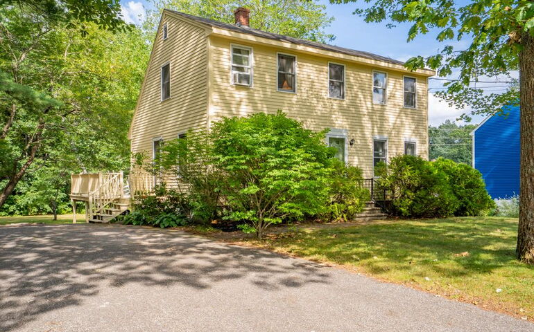 A house with yellow siding has bushes out front.