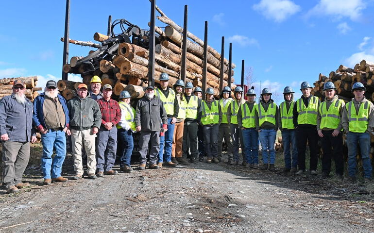 People line up for a photo with a logging truck behind them.