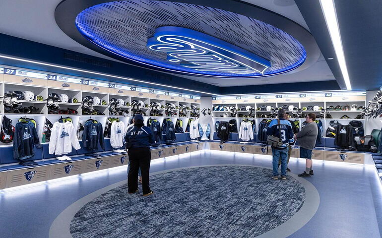 A room has racks of clothes and people standing.