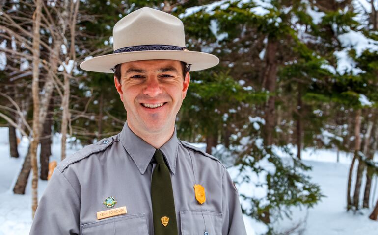 smiling person in ranger uniform and hat in the snowy woods