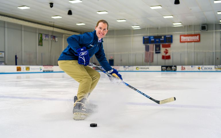 Greg Glynn in an indoor ice rink, in an action shot holding a hockey stick. 