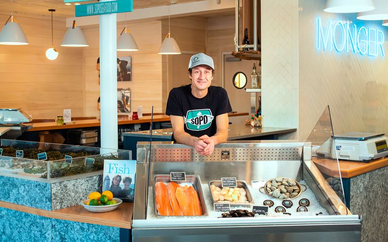 Lucas Myers behind the fish counter at SoPo Seafood. Display shows different kinds of fish and shellfish.