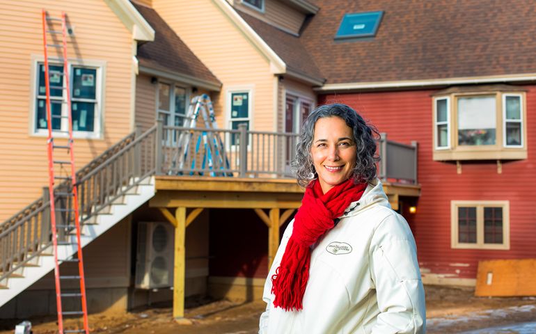 A woman, white, wearing a jacket that says Great Northern Builders, stands in front of an under construction home