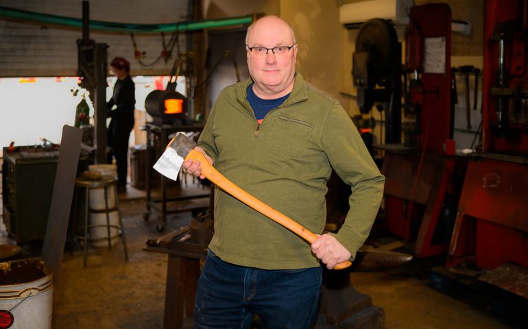 Mark Ferguson holding an axe, with a worker in the background, at the factory.