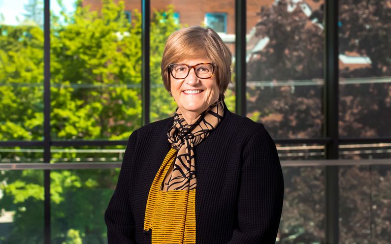 woman with short blonde hair and glasses standing in front of window