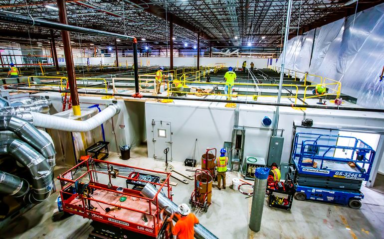 Workers in neon vests and hardhats swarm over construction in a huge warehouse