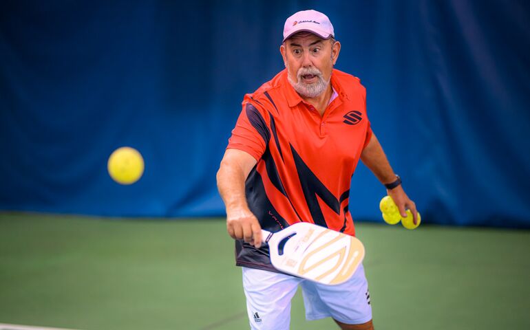 Man playing pickleball, hitting ball with paddle.