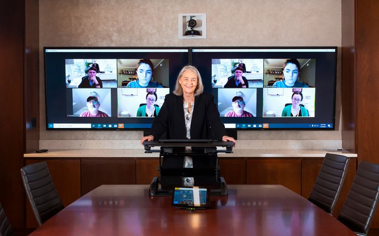 A lawyer standing behind a table with a Zoom screen behind her.