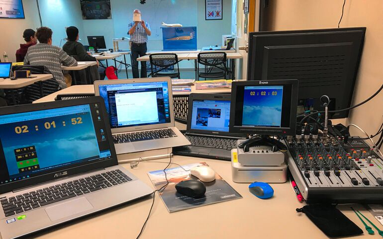 A high-tech classroom with screens that show aviation-related scenes and a male teacher with three adult male and femail students at desks