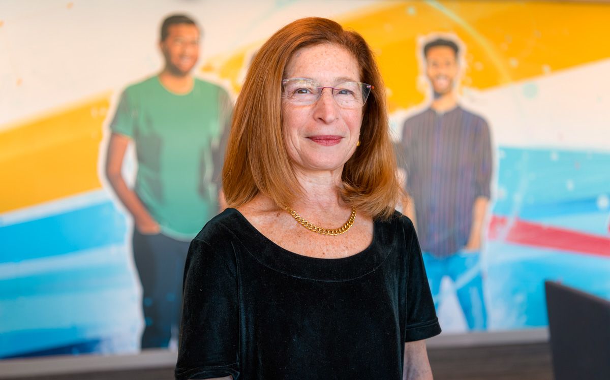 Leslie Hyman standing in front of a mural showing three people.