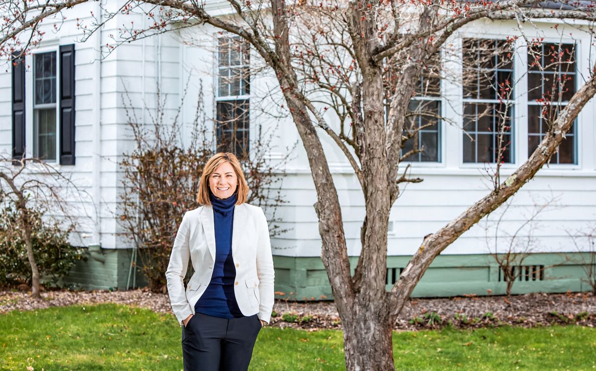 woman in white jacket standing before white house